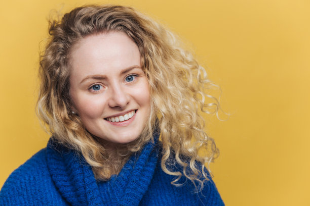 满意快乐的女人有吸引力的外观，愉快的微笑和吸引人的外观，穿着蓝色毛衣，在黄色背景下的姿势。工作室里可爱的年轻女学生模特。图片下载