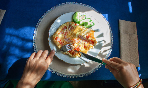 女人的手切着西红柿炒鸡蛋，有流苏的窗帘的影子落在上面，这是阳光明媚的日子里的早餐图片下载