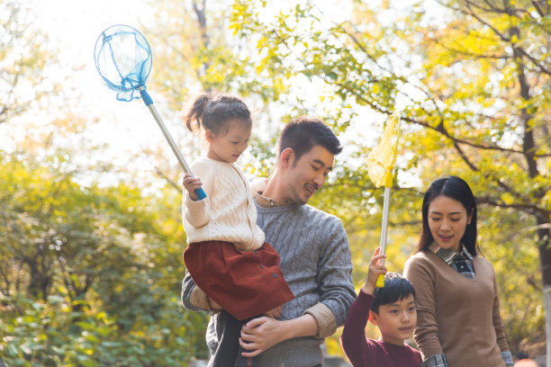 一个年轻的中国四口之家在秋天走在一个森林山涧，小男孩和小女孩与一个昆虫网-库存的照片图片下载