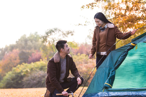 秋季丛林草地上合作搭帐篷的情侣合影图片下载