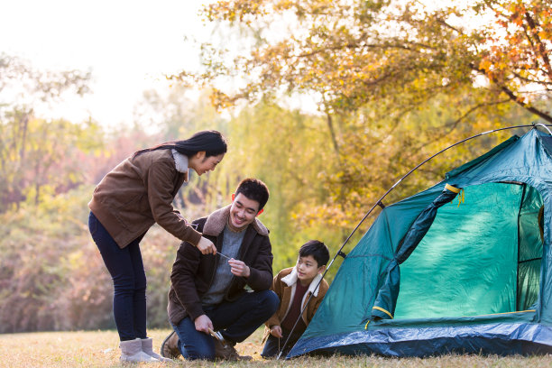 秋天，一家三口在丛林草地上搭起帐篷准备户外露营图片下载