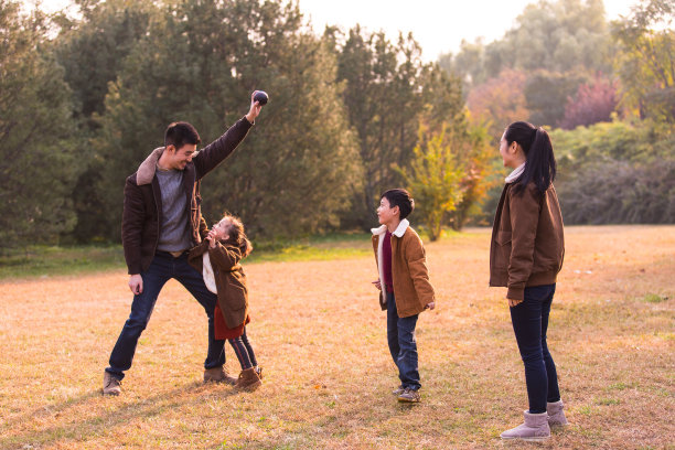年轻的父母和孩子们在秋天的彩色丛林的草地上玩抛球游戏-股票照片图片下载