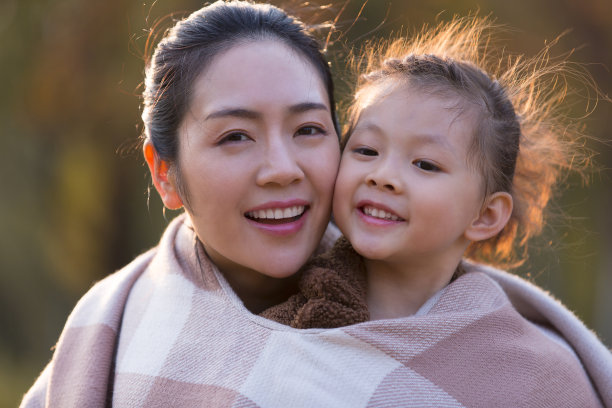 一个年轻的母亲和女儿的脸的特写穿着相同的披肩在秋天的夕阳下彩色的丛林-股票照片图片下载