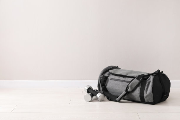 灰色运动包和哑铃放在地板上，靠近浅色的墙壁，为文字留出空间图片下载