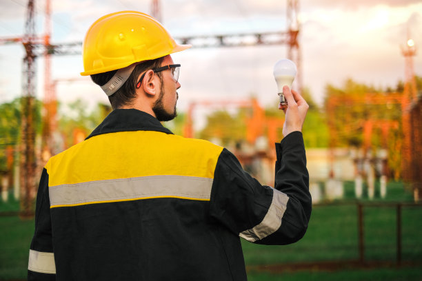 身穿工作服、头戴防护头盔的电工手持灯泡连接照明图片下载
