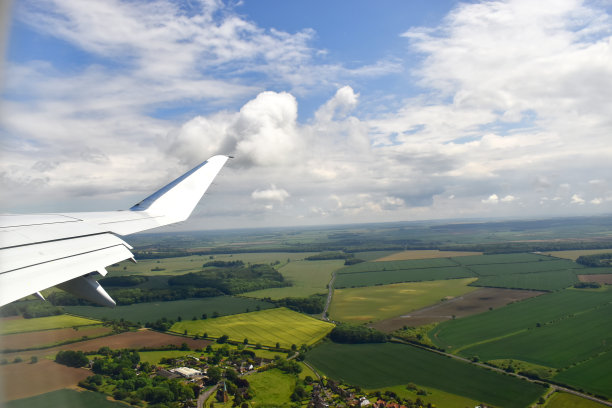 美丽的风景，绿油油的农田下白云漂浮在蓝天。用机翼从飞机窗口看。图片下载