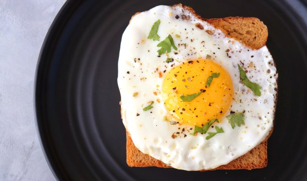 全麦吐司加盐和胡椒粉煎蛋是经典早餐。Sunny单边鸡蛋与黑面包在黑色盘子上的木桌，俯视，复制空间。图片下载