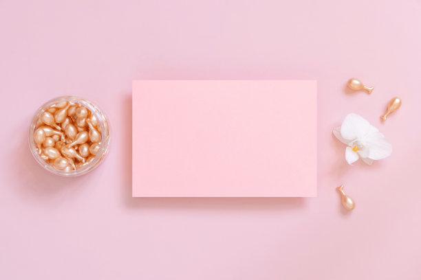 空白卡附近的脸血清胶囊和白色兰花在粉红色的俯视图。模型图片下载