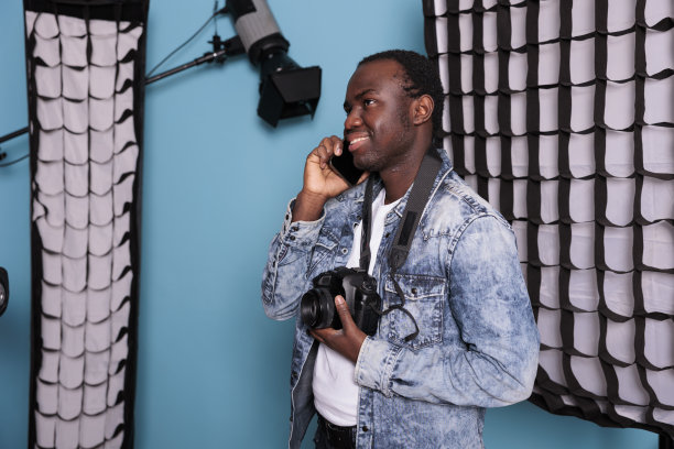 帅气的摄影师站在摄影棚里用智能手机聊天图片下载