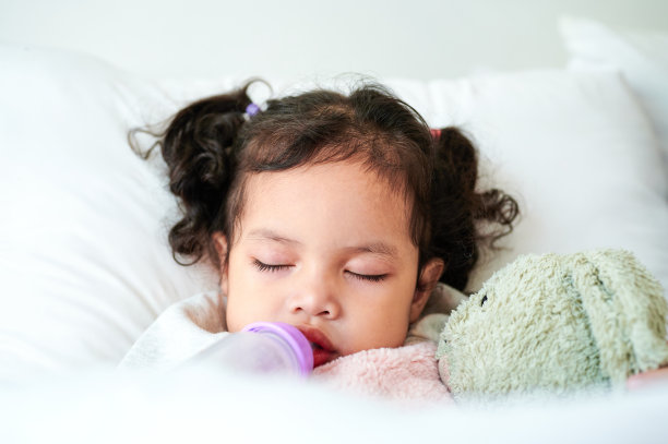 可爱的女孩抱着一瓶牛奶睡在床垫上。图片下载