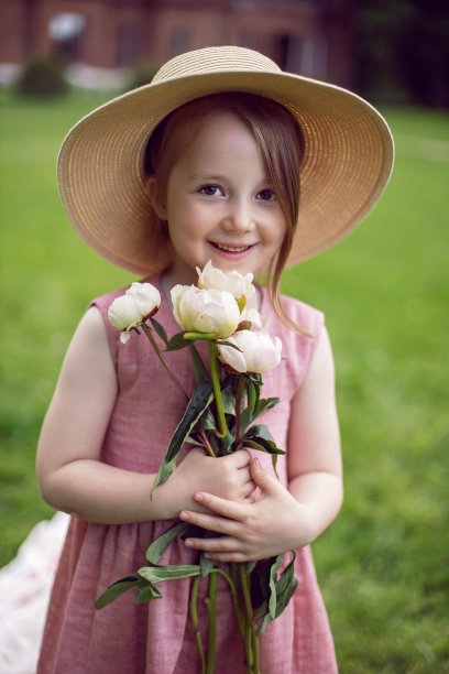 一个美丽的女婴肖像，穿着粉红色的裙子和帽子站在一个绿色的草地上，夏天的花束图片下载