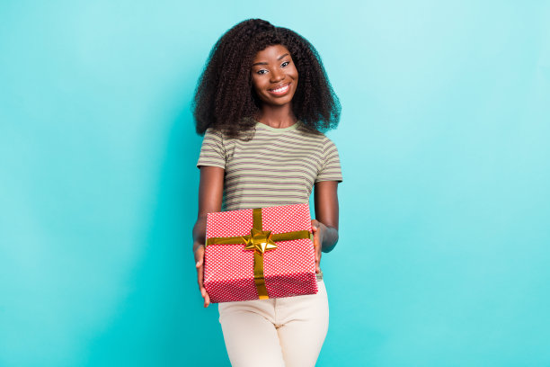 相当积极的人的照片手握礼盒彩带蝴蝶结牙齿微笑孤立在充满活力的翡翠色背景图片下载