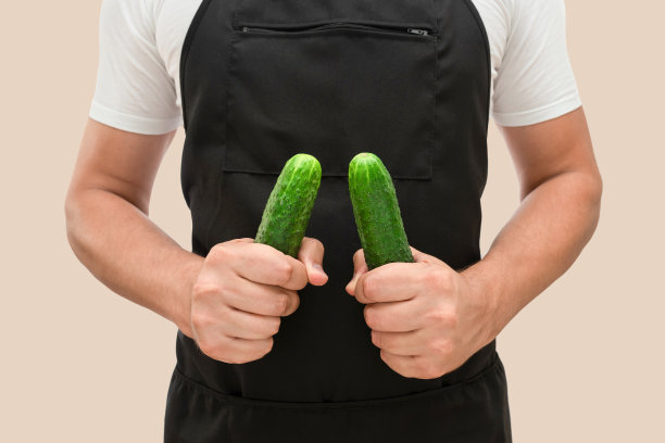 厨师手里拿着鲜黄瓜，放在米色的背景上。烹饪的概念图片下载