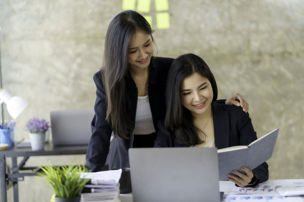 两个年轻的亚洲职业商业女性工作谈话在一个现代创业与笔记本电脑在办公室。图片下载