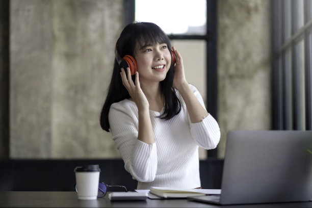 可爱的亚洲女人戴着耳机坐在家里听音乐，开心地享受着听音乐的乐趣。图片下载