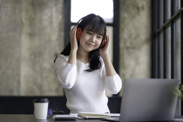 可爱的亚洲女人戴着耳机坐在家里听音乐，开心地享受着听音乐的乐趣。图片下载