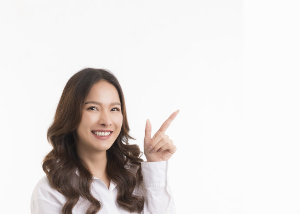 穿着白色衬衫的长头发亚洲女性微笑着用手指着白色的复印空间。图片下载