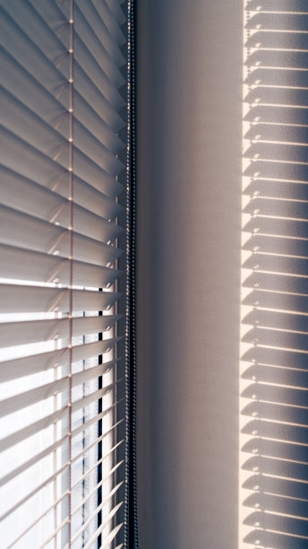 窗户上百叶窗的特写。阳光穿过百叶窗，照在墙上，投射出一道道光影。图片下载