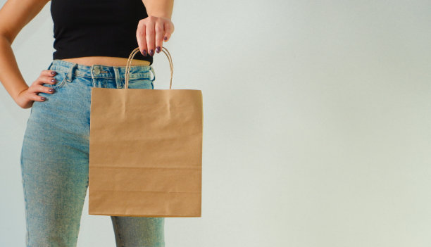 环保的概念。一个穿着蓝色牛仔裤和黑色上衣的迷人女孩手里拿着棕色的牛皮纸包。禁止使用塑料袋。裁剪照片。图片下载