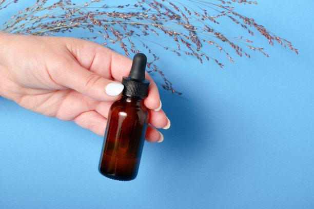 美丽的修饰女人的手与血清瓶在蓝色的背景。美容产品包装图案。美容护肤理念。图片下载