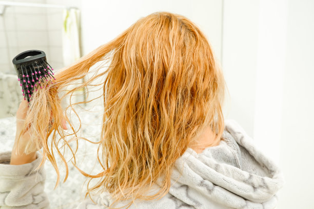 一个金发碧眼的女人在洗澡后试图用梳子梳理她乱糟糟的头发。金色，红色，梳理湿而纠结的头发。图片下载