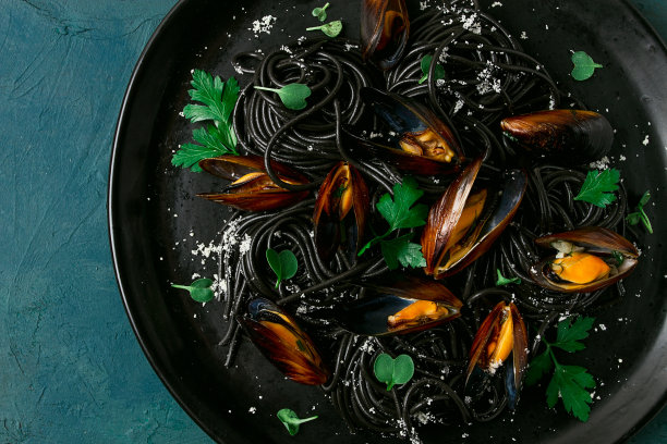 黑鱿鱼意大利面，黑意大利面，煮贻贝，放在黑色盘子里，配上欧芹和帕尔马干酪，特写，选择性聚焦，没有人，图片下载