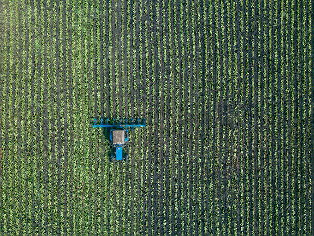 拖拉机在绿色的田野上耙耙。农用拖拉机在田间耕作的鸟瞰图图片下载