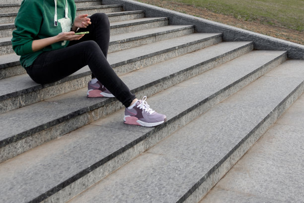 女人坐在楼梯上，手里拿着智能手机图片下载