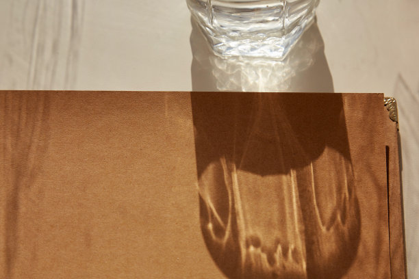 复古仿制的牛皮纸专辑与自然硬阴影。一杯水的影子。前视图。副本的空间。图片下载