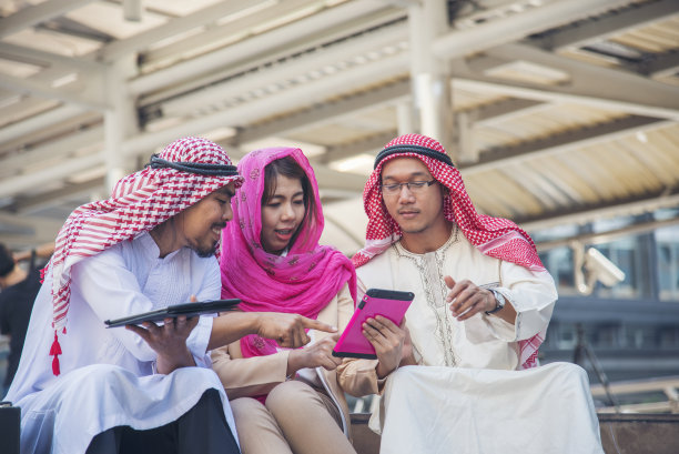 阿拉伯人在阿联酋现代穆斯林城市使用智能平板电脑进行数字营销，触屏讨论。亚洲企业家在户外与老板微笑交谈图片下载