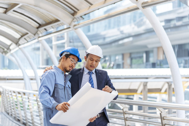 施工工程师身着安全服，团队手持白色黄色安全帽，安全设备在施工现场。土建工程师安全帽保护头。工程概念图片下载