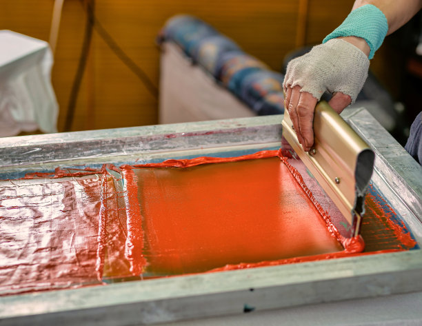 用橡胶滚轴的男性手。丝网印刷生产选择性对焦照片。在设计工作室用丝网法将图案印在衣服上图片下载