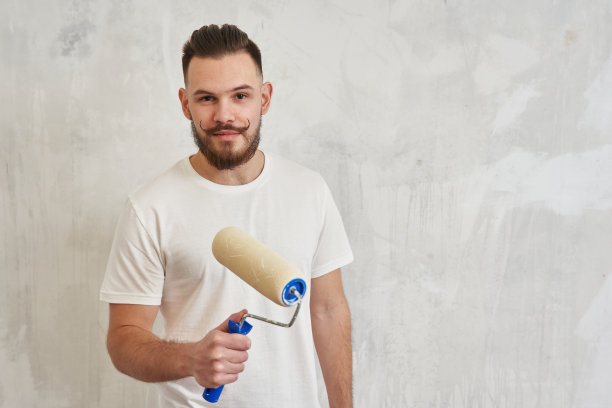 一个留着欢快小胡子的年轻人手里拿着一个油漆滚筒。装修理念，家居装修，墙体彩绘图片下载