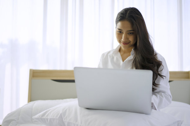一名年轻女子正在使用数码设备。她呆在卧室里。图片下载