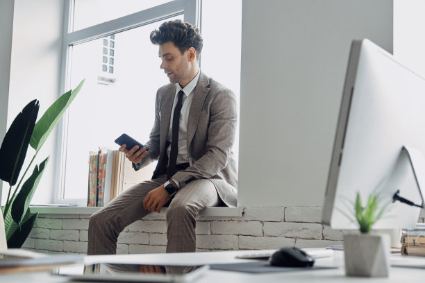 自信的年轻人坐在办公室的窗台上使用智能手机图片下载
