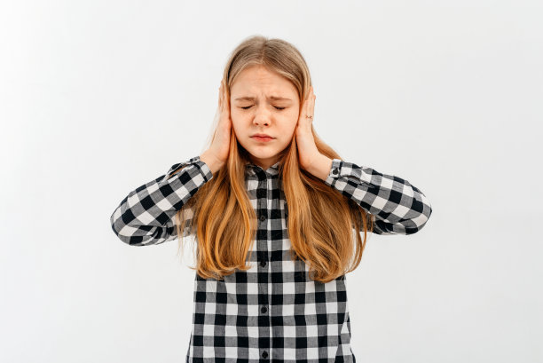 愤怒的少女用手掌捂住耳朵。女孩用手指塞住耳朵，穿着白色背景的休闲衬衫。害怕巨大的声音和令人不快的噪音。图片下载