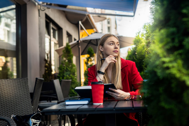 户外露台，一个金发的年轻女人在工作，用钢笔做笔记。图片下载