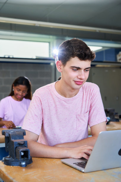 一名年轻的白人男子在高中大学使用笔记本电脑在教室里学习的垂直肖像。图片下载