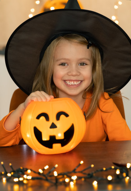 穿着女巫服装的女孩和南瓜灯笼看着相机和微笑。万圣节图片下载