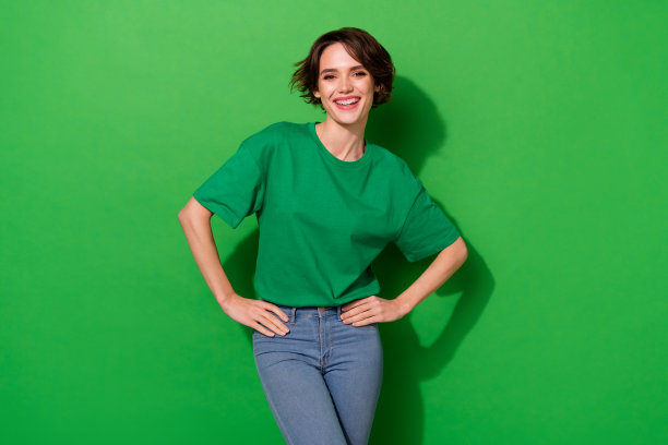 照片时髦迷人的女人穿休闲t恤手手臂腰微笑孤立的绿色背景图片下载
