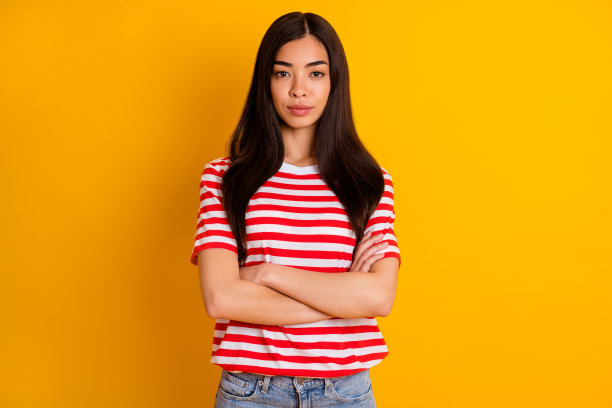 照片迷人自信的年轻女士穿红色衣服手臂折叠孤立黄色背景图片下载