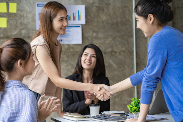 在现代办公室里，亚洲商业伙伴中的女性在会议中握手。一个漂亮的同事友好地微笑，在交易完成后握手，朋友们鼓掌。图片下载