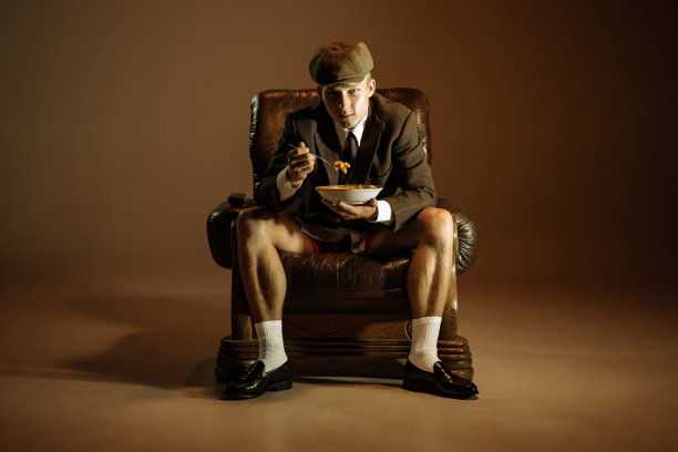 年轻人，复古的20世纪20年代风格的英国黑帮穿着西装和帽子品尝意大利面孤立在黑暗的vintage背景。商业、家庭、艺术、时尚图片下载