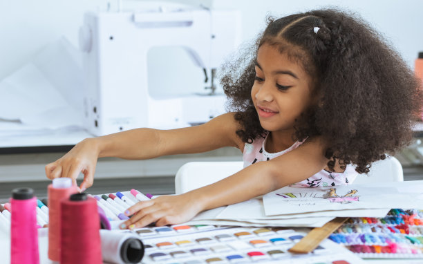 可爱的非洲小女孩在裁缝室的纸上画画或素描服装设计，舒适的家是她的职业梦想，微笑着幸福和乐趣。休闲，生活方式，教育，儿童概念。图片下载
