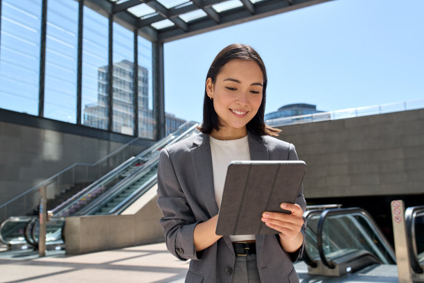 微笑的亚洲年轻女商人站在城市地铁里用平板电脑。图片下载