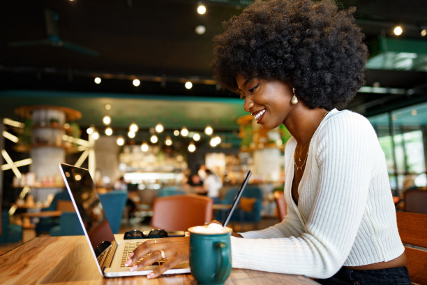 微笑的非洲年轻女性坐在咖啡馆的笔记本电脑图片下载