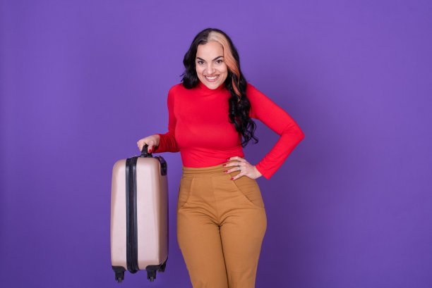 迷人的女旅行者拿着她的手提箱对着紫色的背景。图片下载