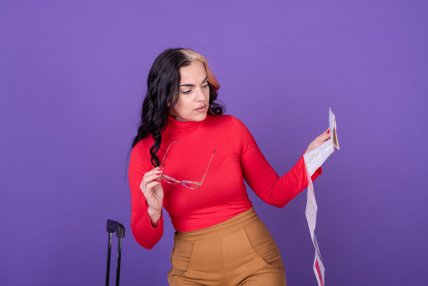 年轻女子带着行李箱旅行，在紫色的背景下看地图。影棚拍摄。图片下载