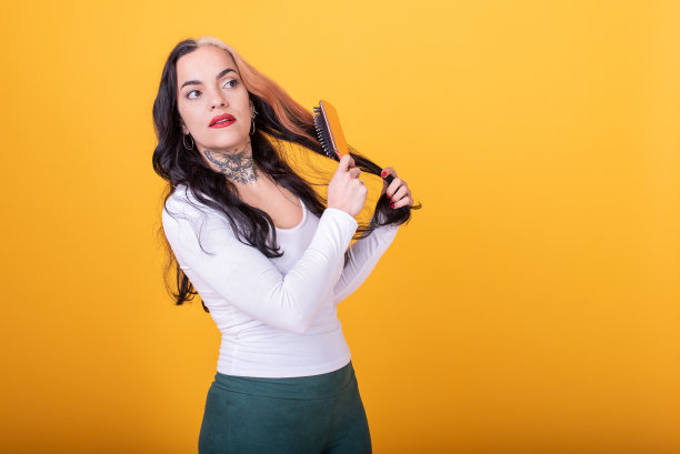 迷人的女人梳理她的头发在黄色的背景。图片下载