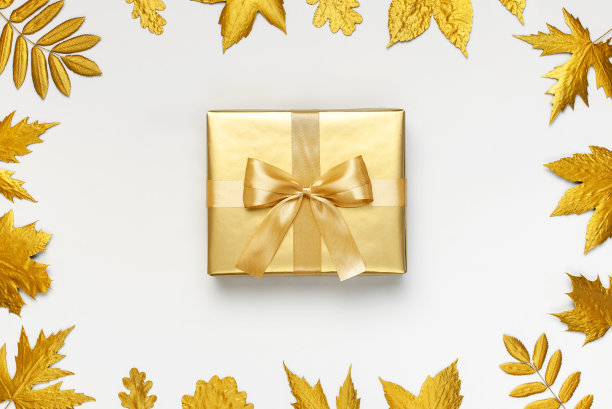 平铺秋日假日概念。金色的礼物或礼品盒与丝带和金色的秋叶在浅灰色的背景俯视拷贝空间。惊喜，祝贺，生日，贺卡图片下载